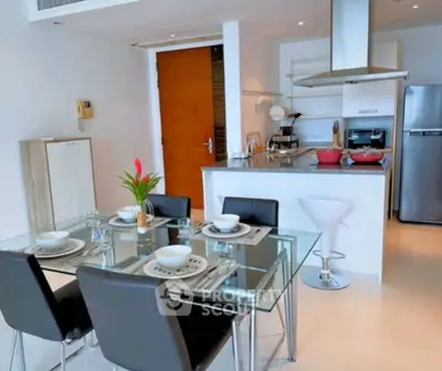 Modern open-layout kitchen and dining area with sleek glass table and stainless steel appliances.