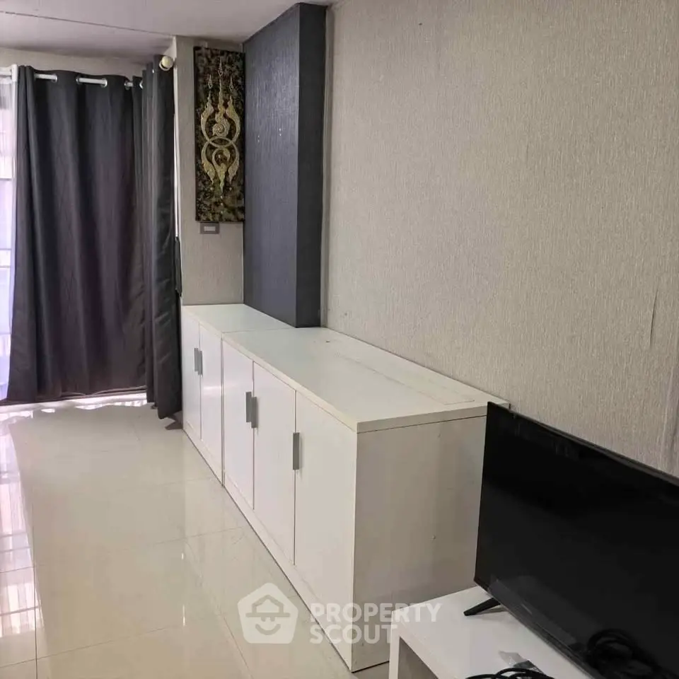 Modern living room with sleek white cabinets and flat-screen TV, featuring elegant curtains and wall art.