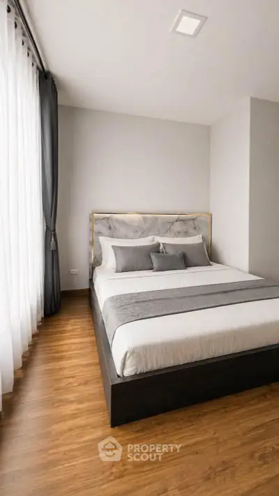 Modern bedroom with elegant decor and wooden flooring, featuring a stylish bed and large window with curtains.