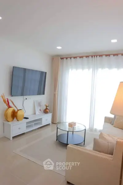 Elegant living room with modern decor, large TV, and natural light through sheer curtains.