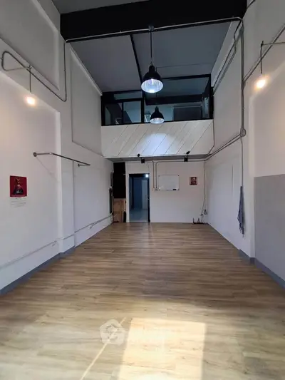 Spacious industrial-style room with high ceilings and wooden flooring, ideal for creative studio or office space.