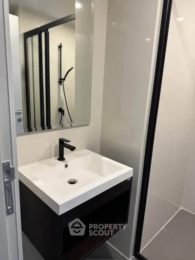 Modern bathroom with sleek sink and shower, featuring contemporary fixtures and minimalist design.