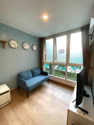 Cozy living room with blue sofa, wall clocks, and large window view in modern apartment.