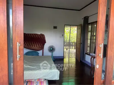 Charming bedroom with wooden floors and balcony access, offering a serene view of lush greenery.