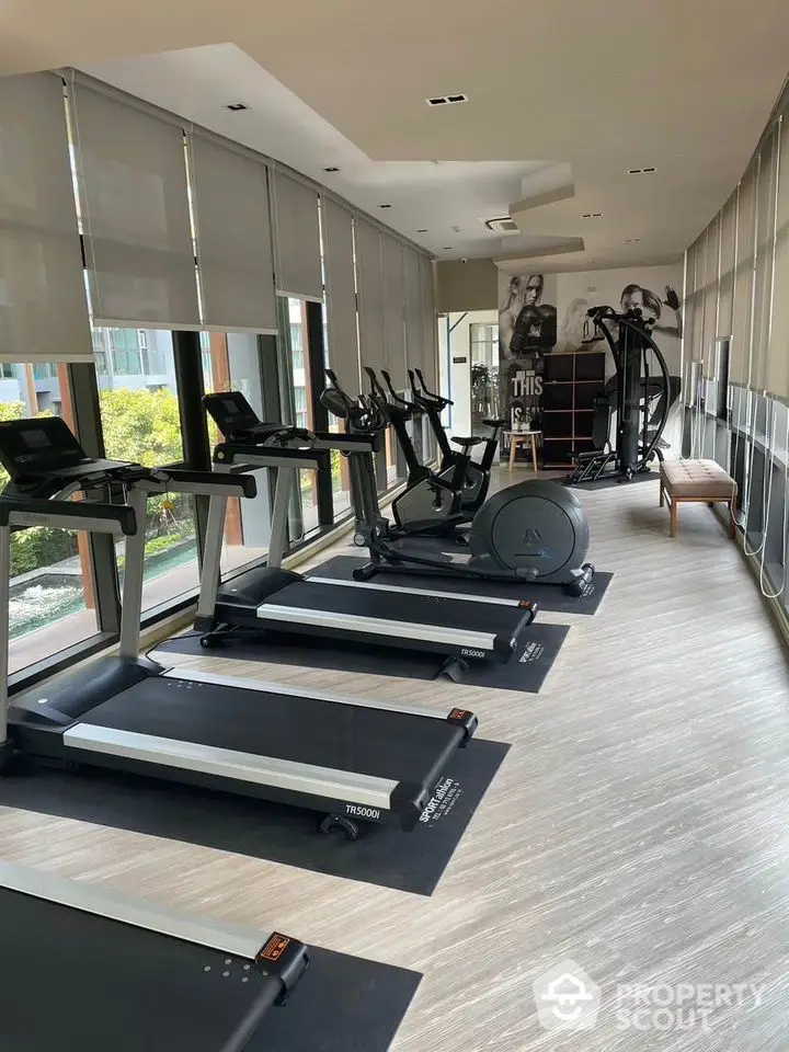 Modern gym with treadmills and exercise equipment in a bright, spacious room with large windows.