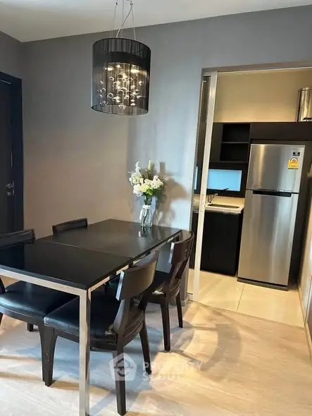 Modern dining area with sleek black table and chairs, adjacent to a compact kitchen with stainless steel appliances.