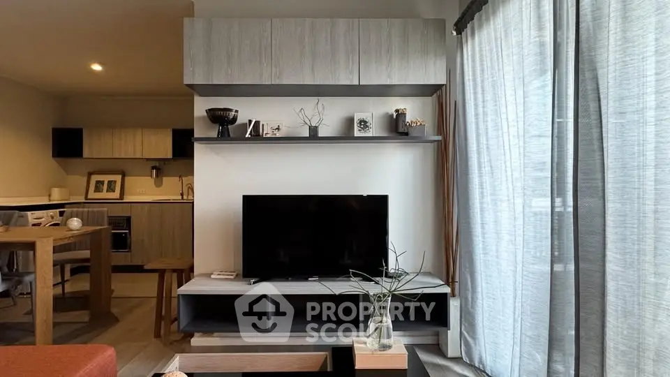 Modern living room with stylish decor and open kitchen layout, featuring a sleek TV setup and natural light.