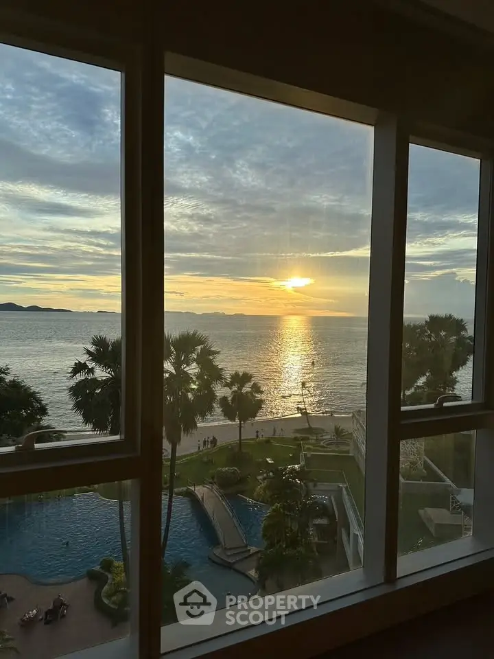 Stunning ocean view from a high-rise window overlooking a pool and palm trees at sunset.