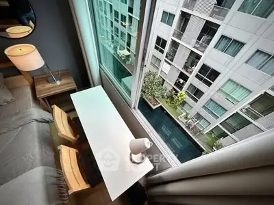 Modern bedroom with large window overlooking pool and neighboring building, featuring sleek desk and lamp.