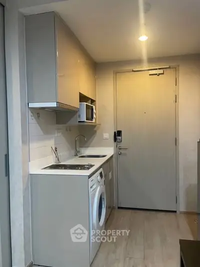 Compact kitchen with washing machine and microwave in modern apartment