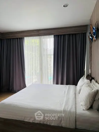 Spacious bedroom with large windows and elegant curtains, offering a serene and comfortable living space.