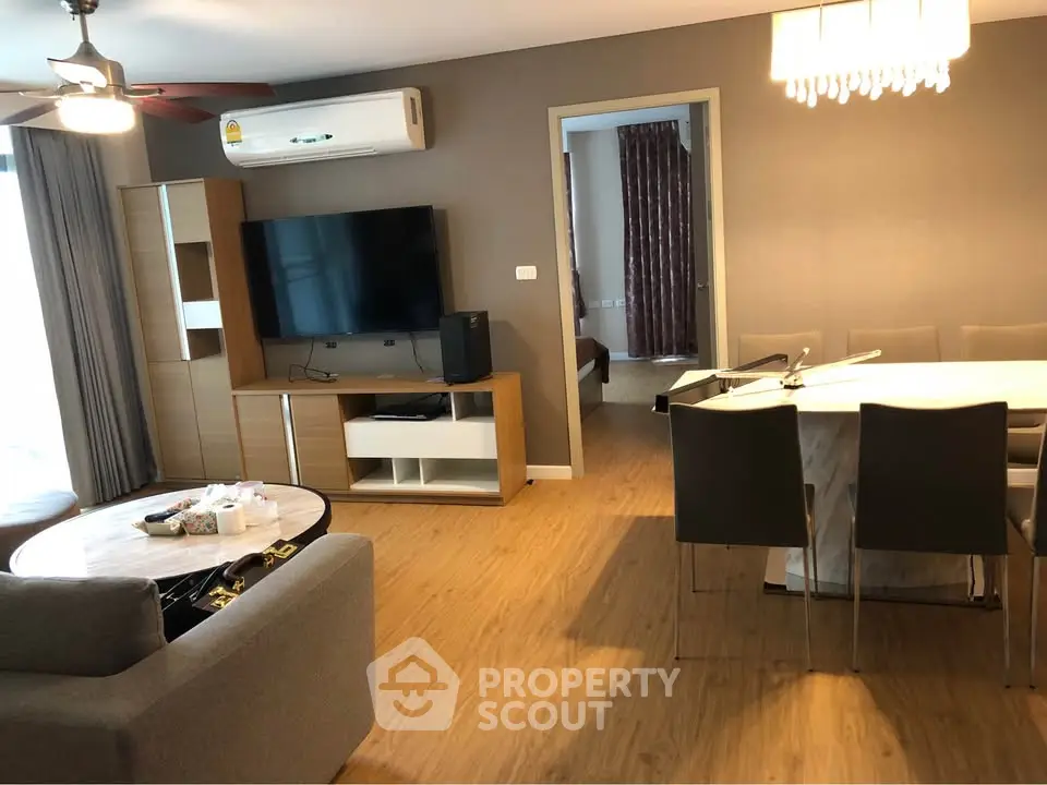 Spacious living room with modern decor and open layout, featuring a large TV and elegant dining area.