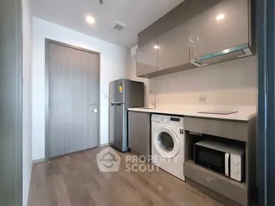 Modern kitchen with washing machine, microwave, and sleek cabinetry in compact layout.