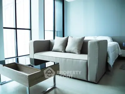 Modern bedroom with stylish sofa and glass coffee table, featuring floor-to-ceiling windows.