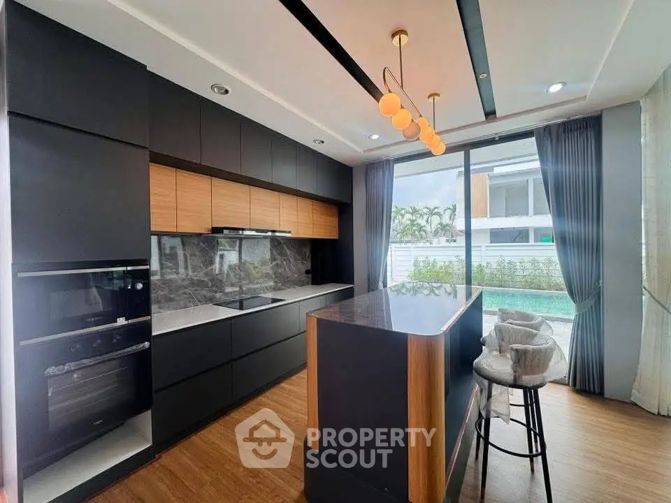 Modern kitchen with sleek black cabinetry, marble backsplash, and pool view, featuring elegant lighting and bar seating.