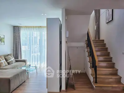 Modern living room with staircase and large window, featuring cozy seating and stylish decor.