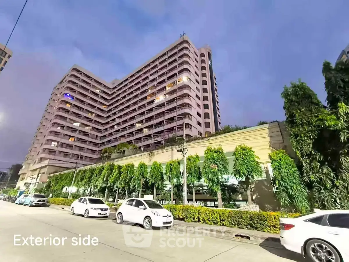 Stunning high-rise building exterior with lush greenery and ample parking space at dusk.
