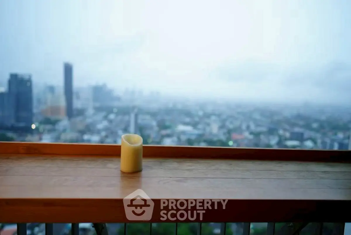 Stunning cityscape view from a high-rise balcony with wooden railing and candle.