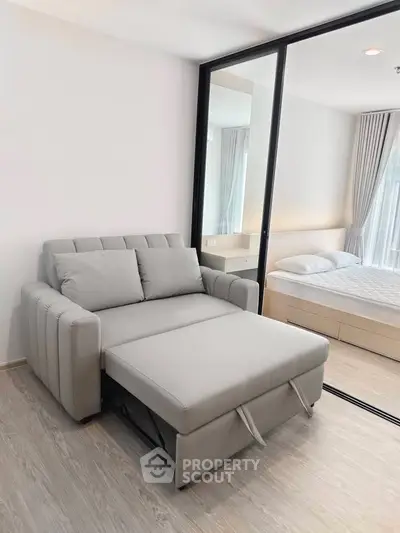 Modern apartment with convertible sofa and cozy bedroom separated by glass partition.