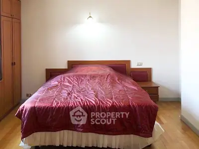 Cozy bedroom with wooden furniture and elegant red bedding, perfect for relaxation.