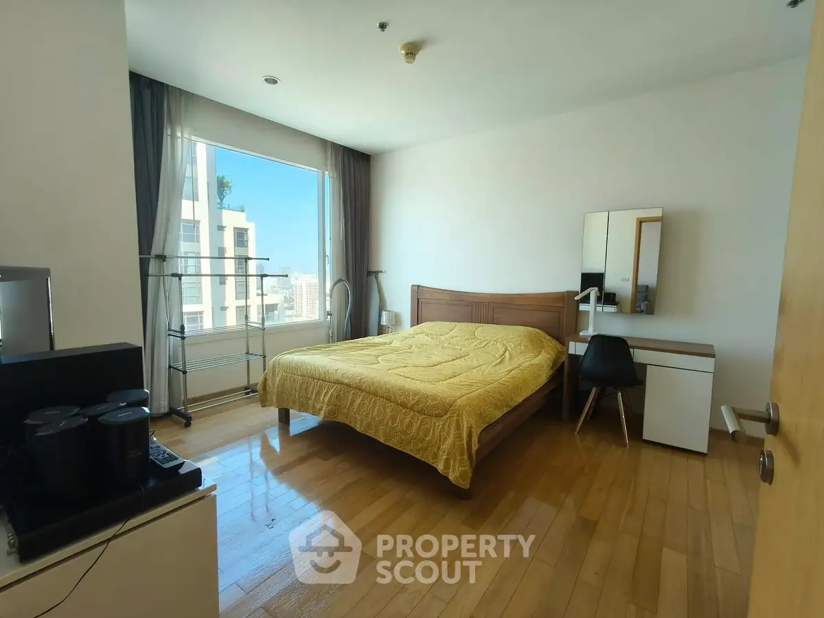 Spacious bedroom with wooden flooring and large window offering city views