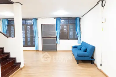 Spacious living room with blue sofa and wooden flooring, featuring large windows and elegant curtains.