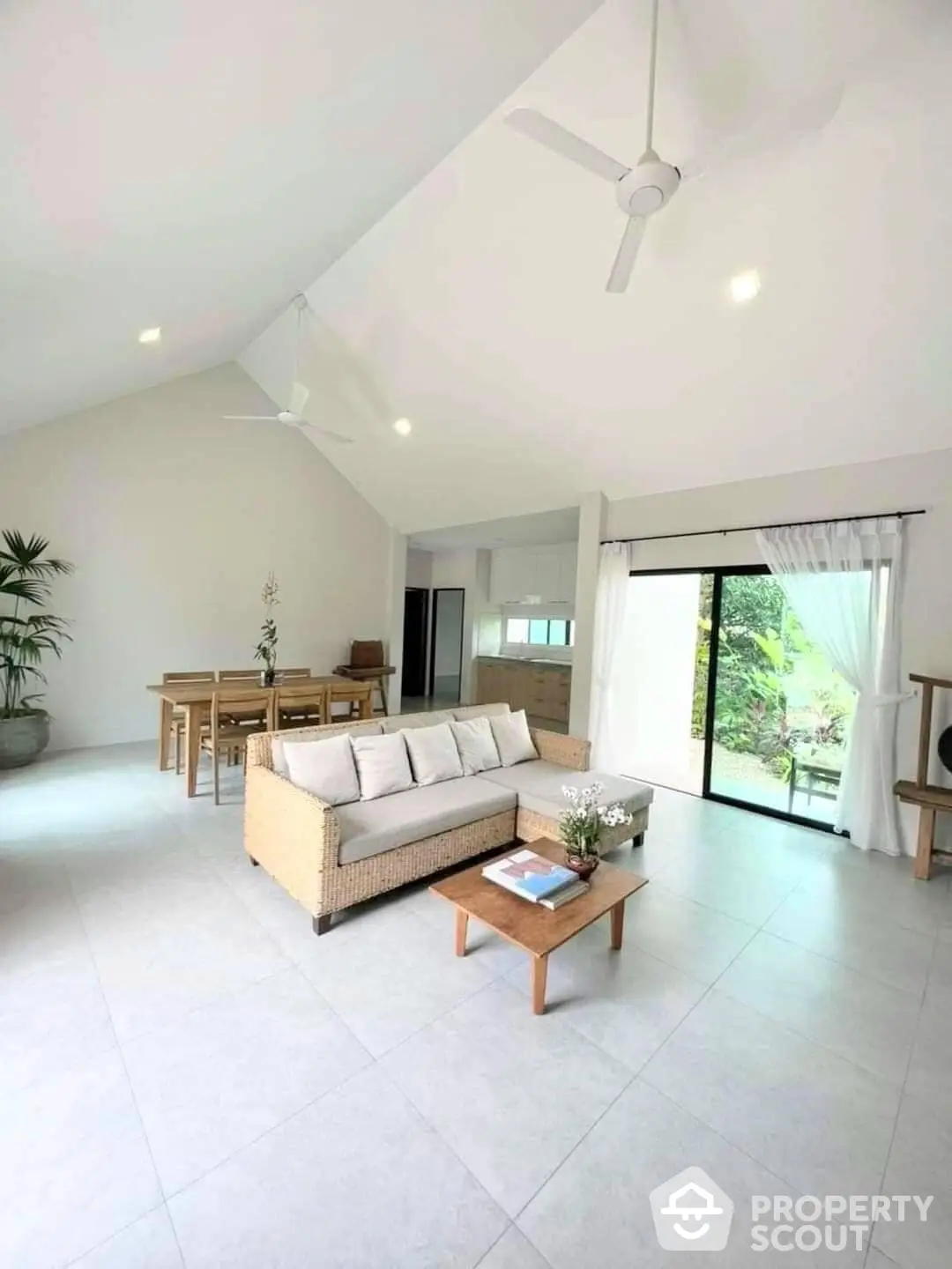 Spacious living room with high vaulted ceiling, large windows, and modern furnishings, opening to a serene outdoor view.