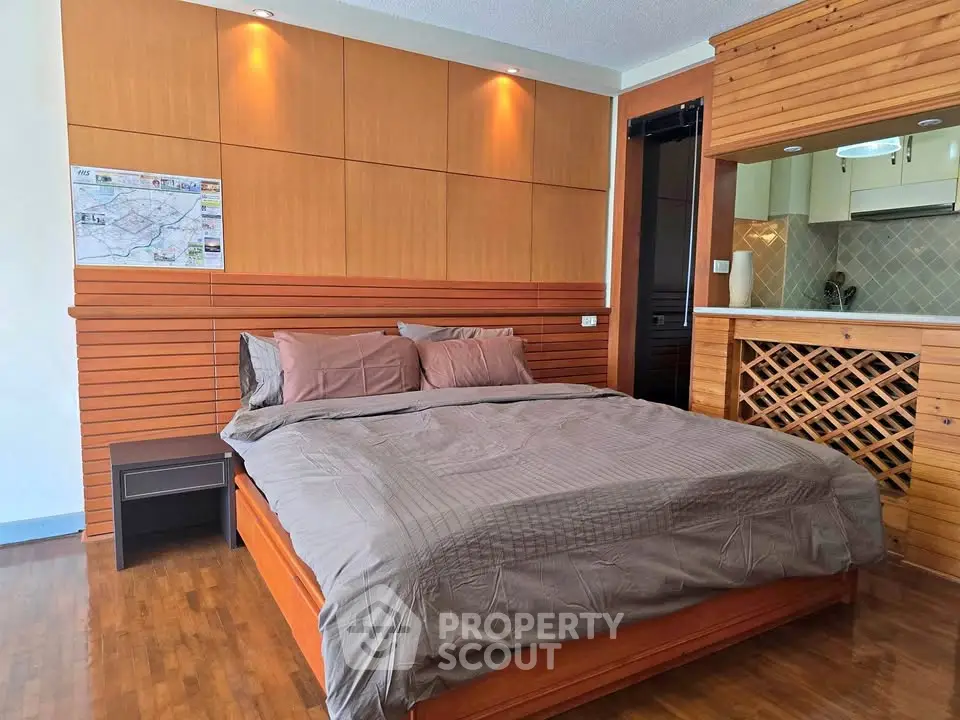 Cozy bedroom with wooden accents and adjacent kitchen area in modern apartment.