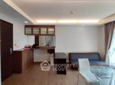 Modern living room with sleek furniture and natural light, featuring a glass dining table and cozy seating area.