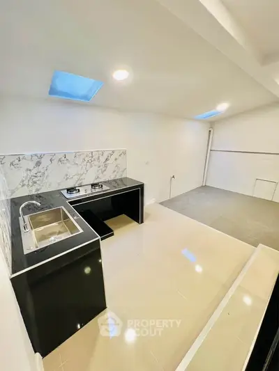 Modern kitchen with sleek black countertops and gas stove, featuring skylights and spacious layout.