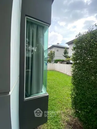 Modern house exterior with large window and lush green lawn, perfect for family living.
