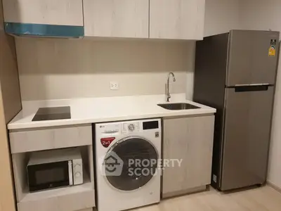 Modern kitchen with sleek appliances including washing machine, microwave, and fridge in compact layout.
