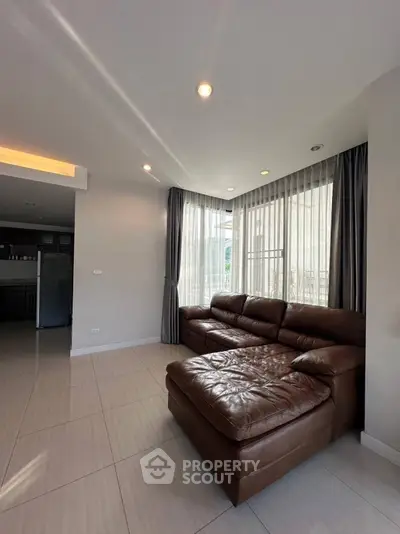 Spacious living room with leather sectional sofa and large windows in modern apartment