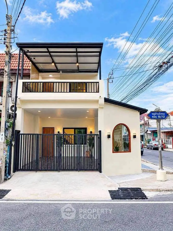 Modern two-story house with balcony and gated entrance on a sunny day.