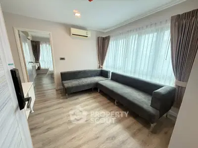 Modern living room with sleek grey sofa and large windows, featuring elegant curtains and wooden flooring.