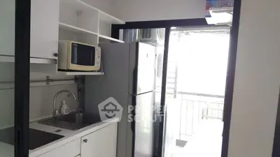 Compact kitchen with microwave and fridge leading to a bright balcony