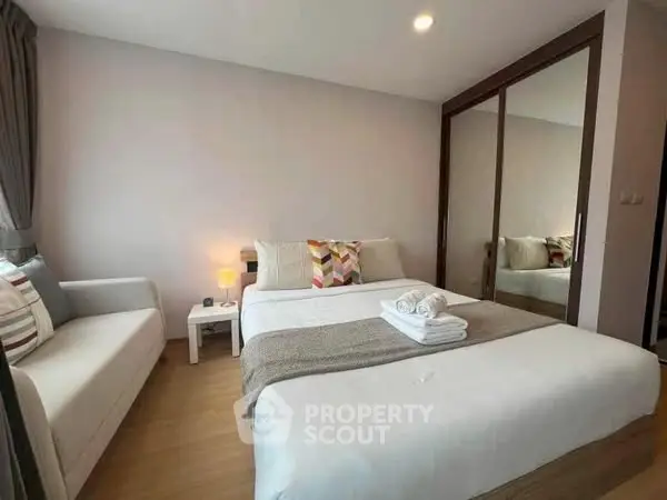 Modern bedroom with cozy bed, stylish sofa, and mirrored wardrobe in a bright apartment.