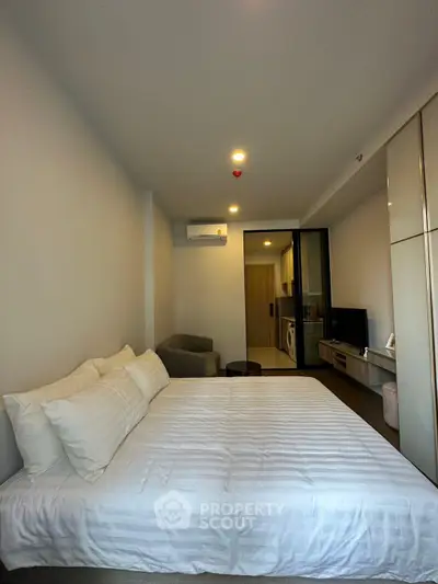 Modern bedroom with cozy bed, air conditioning, and open view to living area with washing machine.