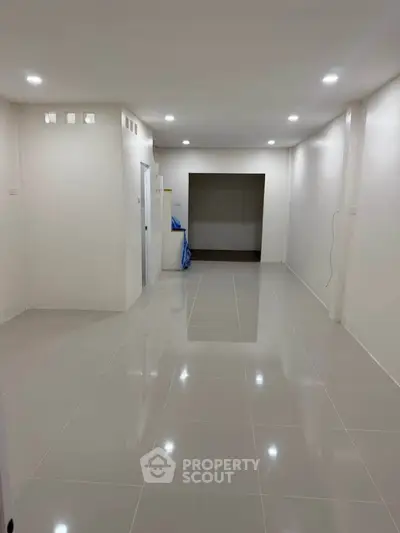 Spacious empty room with glossy tiled flooring and recessed lighting, ideal for customization.