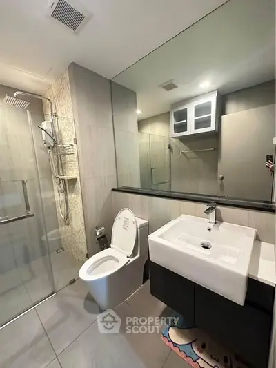 Modern bathroom with glass shower, sleek vanity, and large mirror in contemporary apartment.