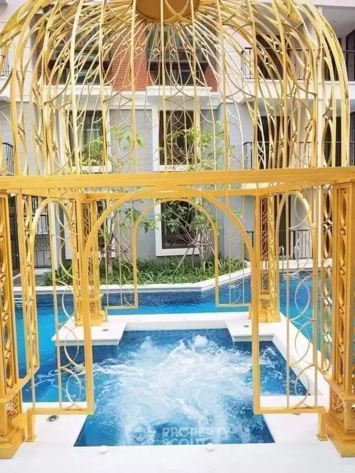 Luxurious pool area with ornate golden gazebo and lush greenery in modern building complex.