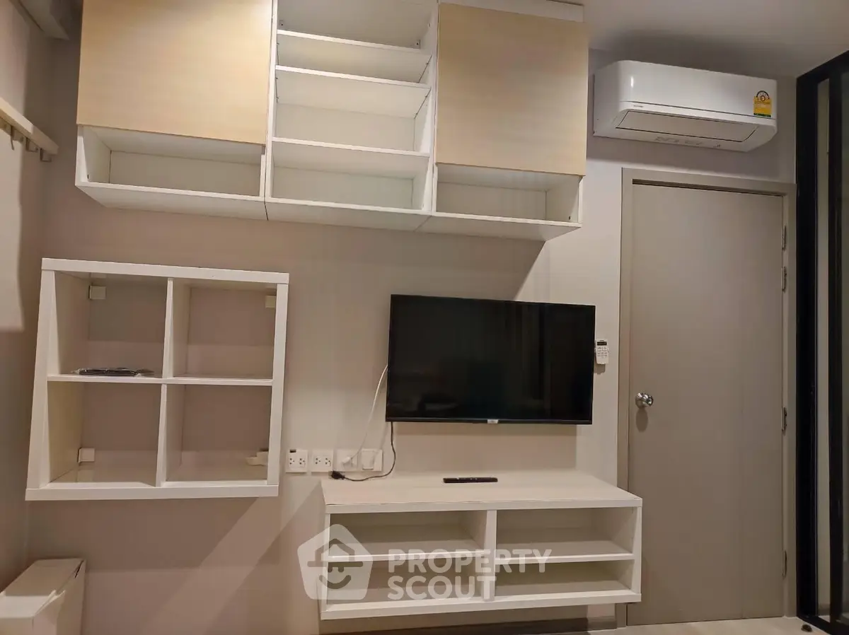 Modern living room with wall-mounted TV and sleek storage units, featuring a minimalist design and air conditioning.