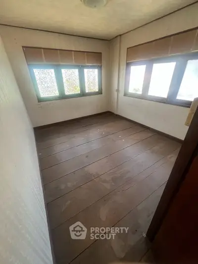Cozy room with wooden flooring and large windows, perfect for a home office or small bedroom.