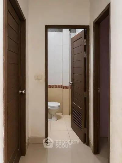 Compact bathroom with wooden door and tiled walls in a cozy apartment.