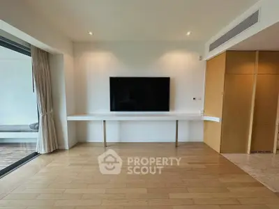 Spacious modern living room with wooden flooring and large TV, perfect for entertainment.
