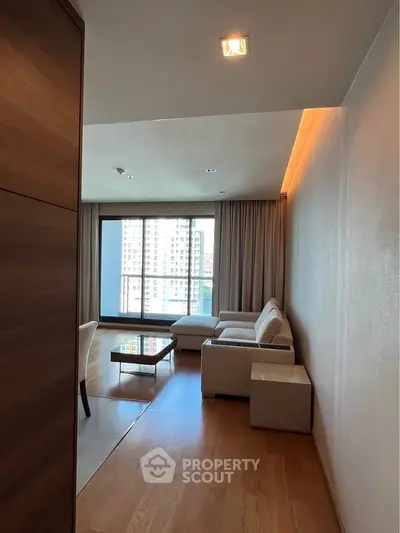 Spacious modern living room with large windows and city view, featuring elegant furniture and wooden flooring.