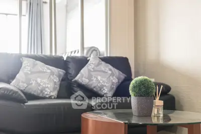 Modern living room with stylish black leather sofa and decorative cushions, featuring a glass coffee table with plant decor.