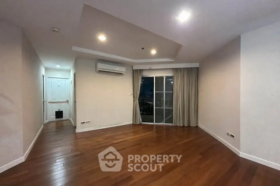 Spacious living room with wooden flooring and balcony access in modern apartment.