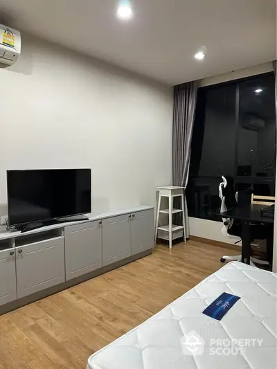 Modern bedroom with TV and study area, featuring sleek furniture and large window.