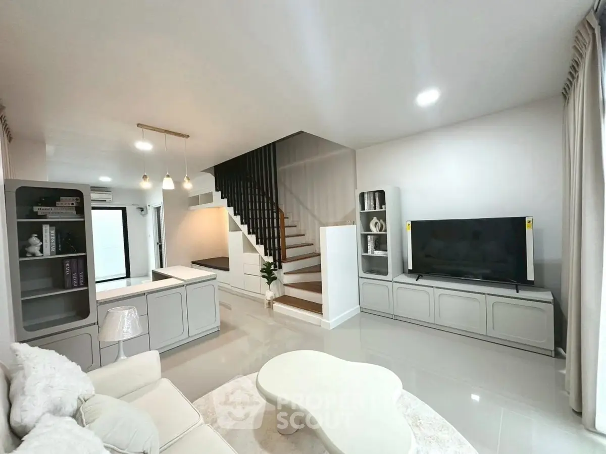Modern living room with sleek design, featuring a cozy sofa, stylish staircase, and large flat-screen TV.